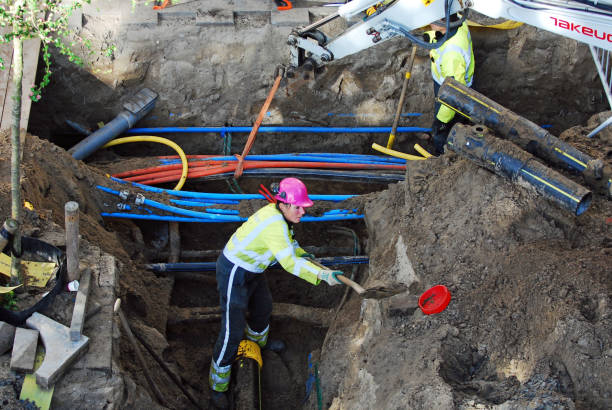 Utility female worker digging around a trench with her shovel  in the street of Amsterdam to install a new electric cable and optical fibre.